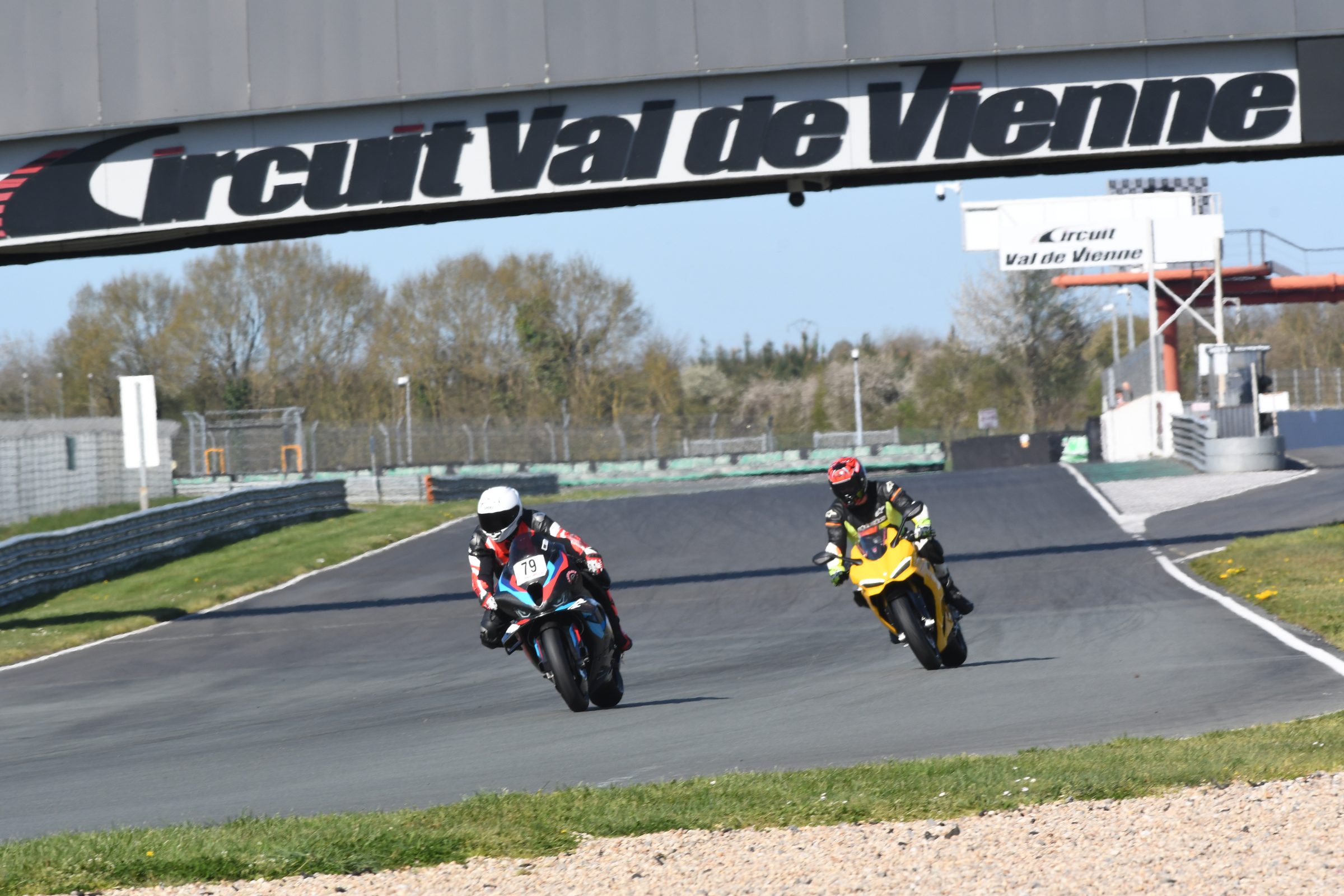 Twee motorrijders op de baan onder de brug van Circuit du Val de Vienne