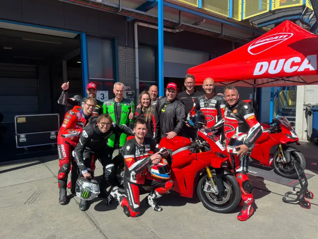 Groepsfoto van rijders en het Ducati-team bij een rode Ducati voor de pitbox