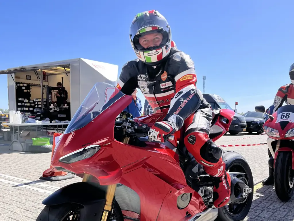 Rijder in racepak op een rode Ducati Panigale in de paddock tijdens een circuitdag